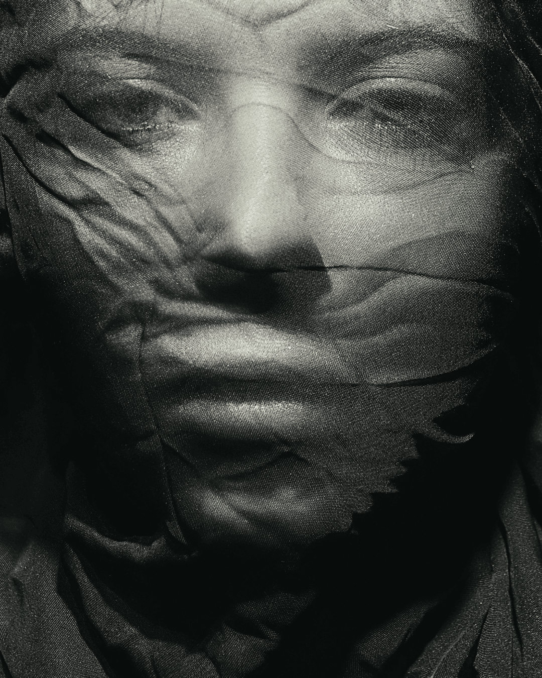 Editorial portrait of a woman behind dark sheer fabric