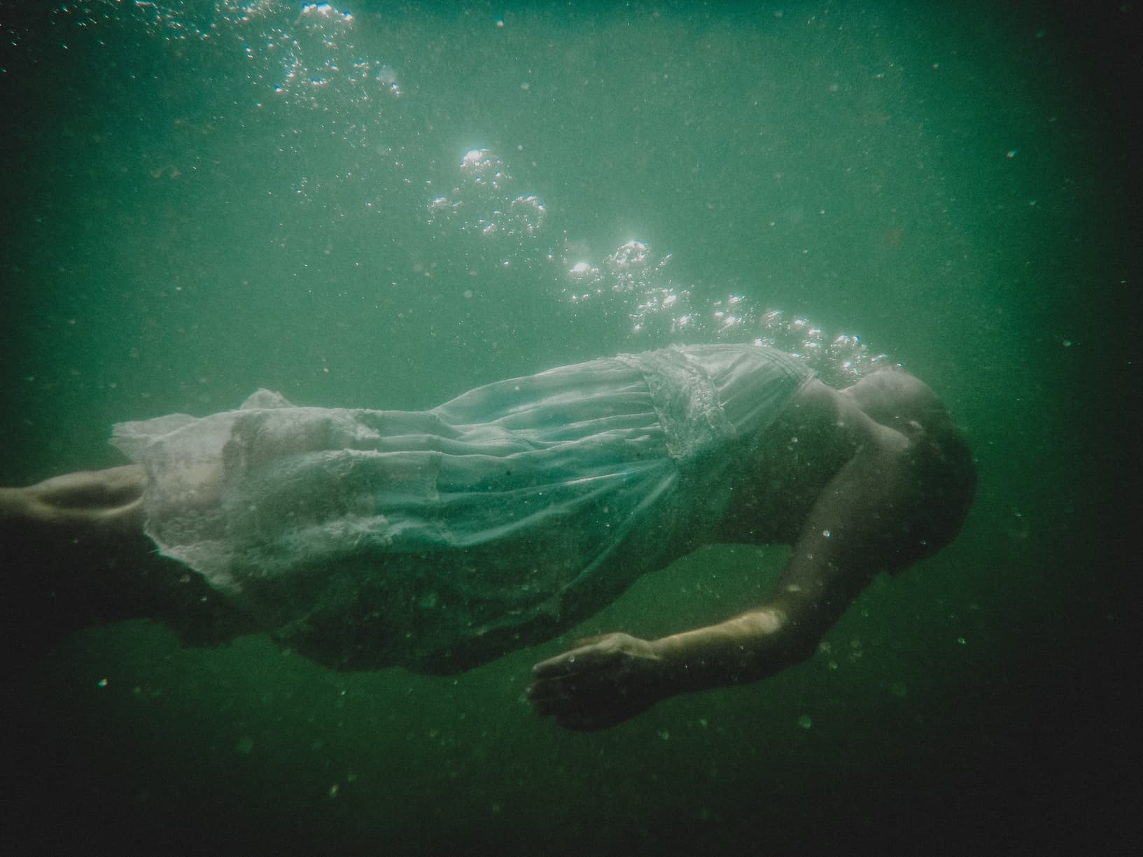 Figure in flowing green fabric underwater, evoking fluid movement and renewal